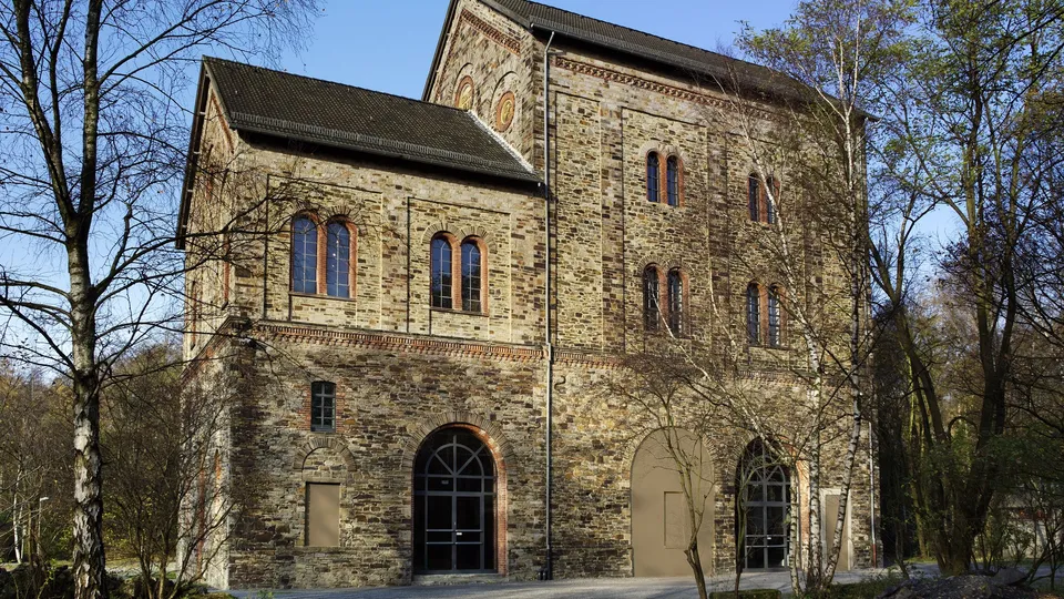 Backsteingebäude des Museums Industriekultur in Osnabrück mit Bögen und Fenstern, umgeben von Bäumen.