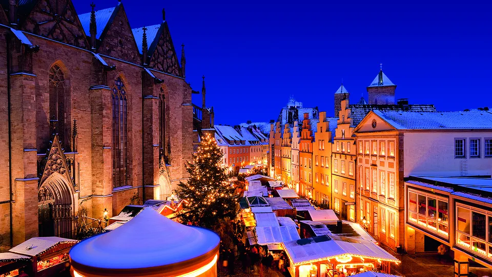 Weihnachtsmarkt in winterlicher Atmosphäre mit hell erleuchteten Ständen und einer historischen Kirche.