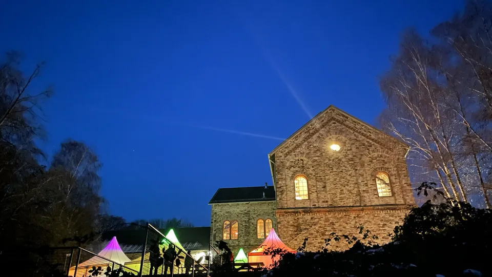 Ein historisches Backsteingebäude beleuchtet den Nachthimmel; bunte Lichter im Vordergrund.