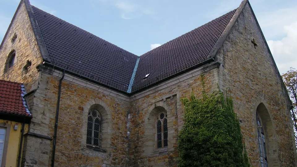 Historische Kirchenmauer aus Backstein, flankiert von Fenstern mit gotischem Stil, bewachsen mit Efeu.