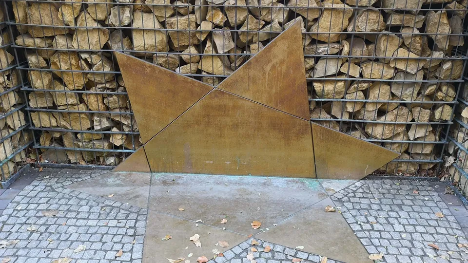 Ein zerbrochener Davidstern auf Kies; Symbol für zerstörtes jüdisches Leben vor einer Steinwand.